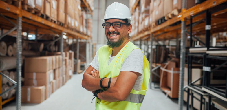 Man in hard hat and high vis vest in a warehouse smiling at camera