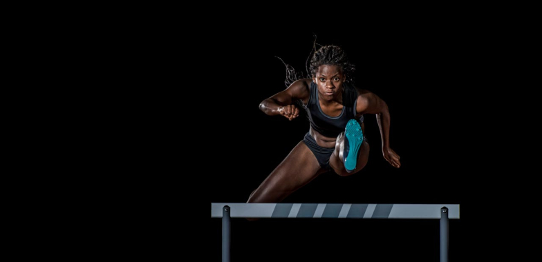 Female athlete running towards camera jumping a hurdle