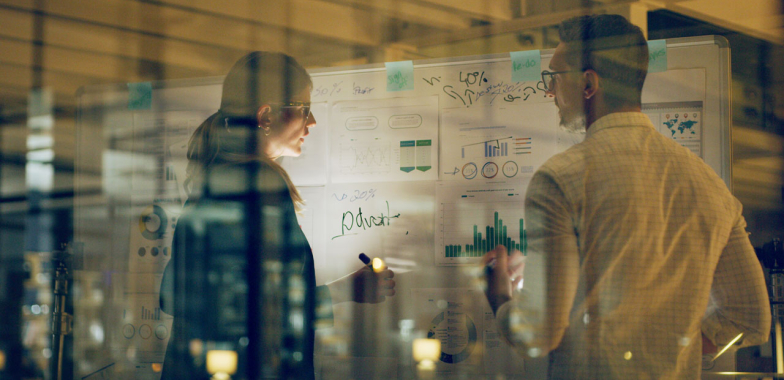 Two people standing looking at a white board in low light