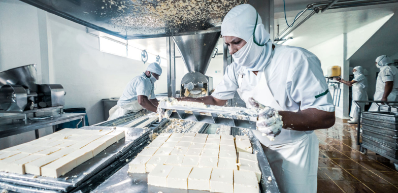 Person in full PPE working in a cheese factory slicing feta 