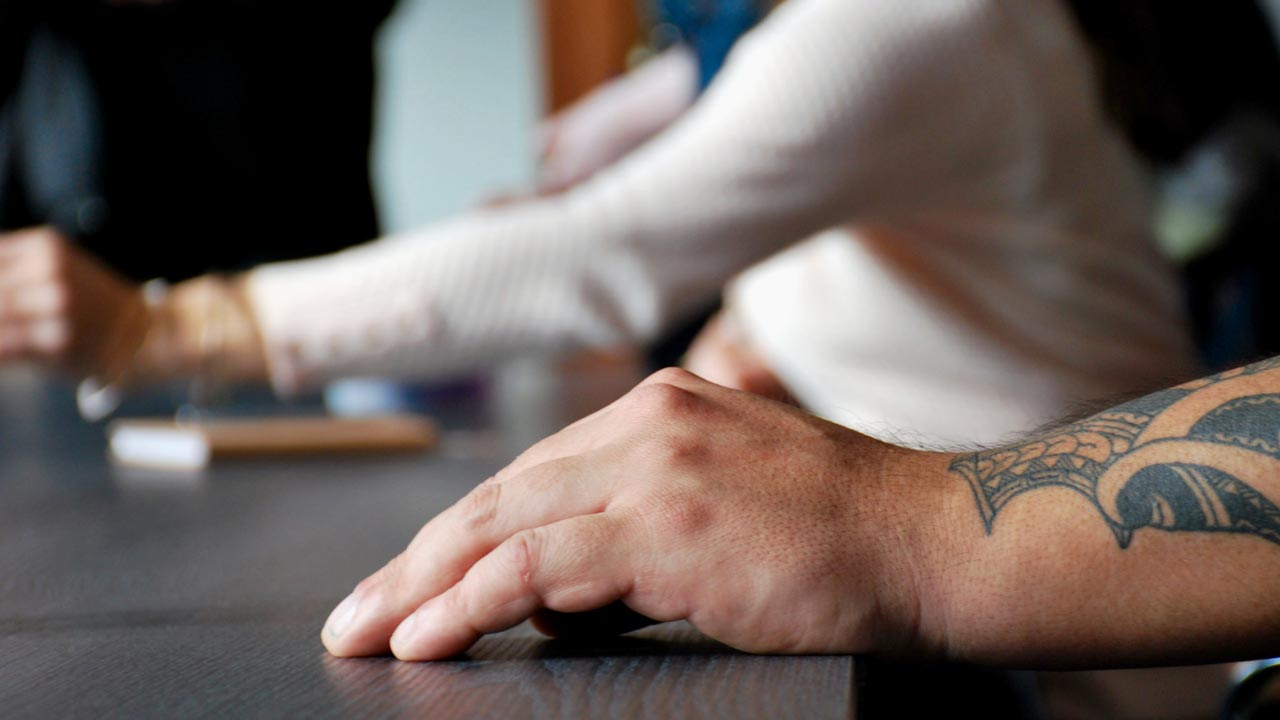 Arm with tatoos resting on a table with other people in background