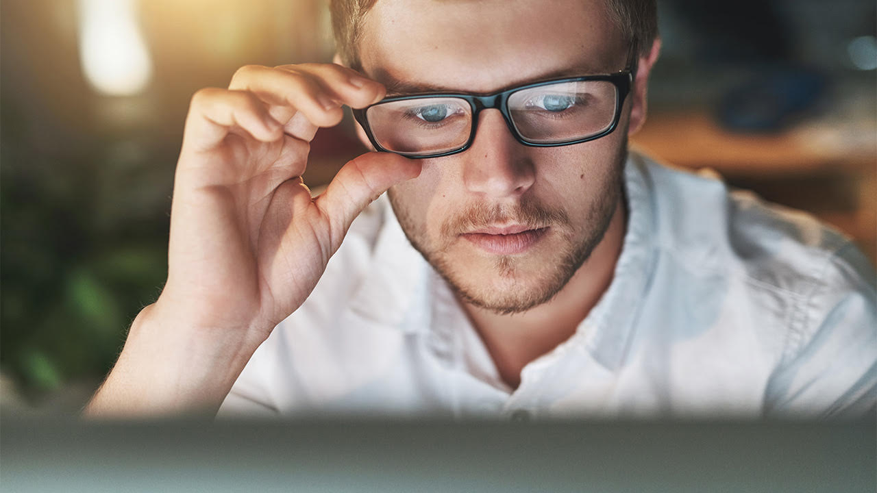 Man looking at computer screen while adjusting his glasses