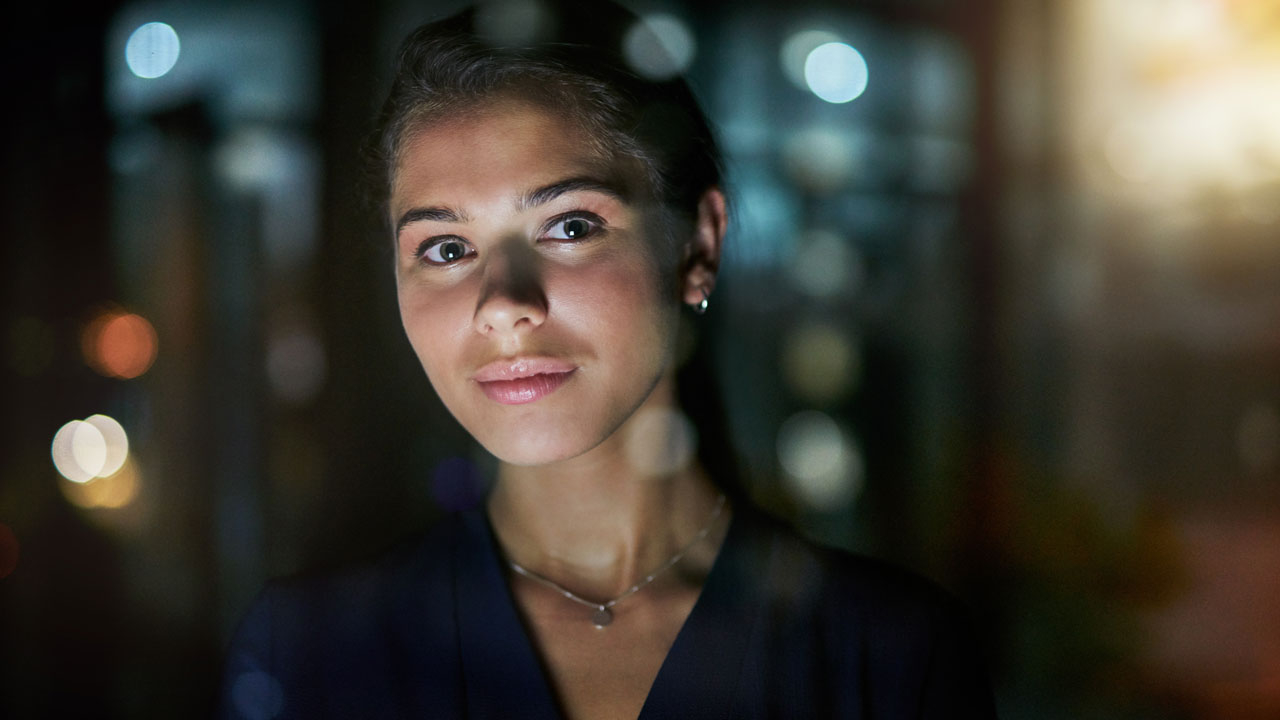 Woman with dark background looking at camera, head and shoulders
